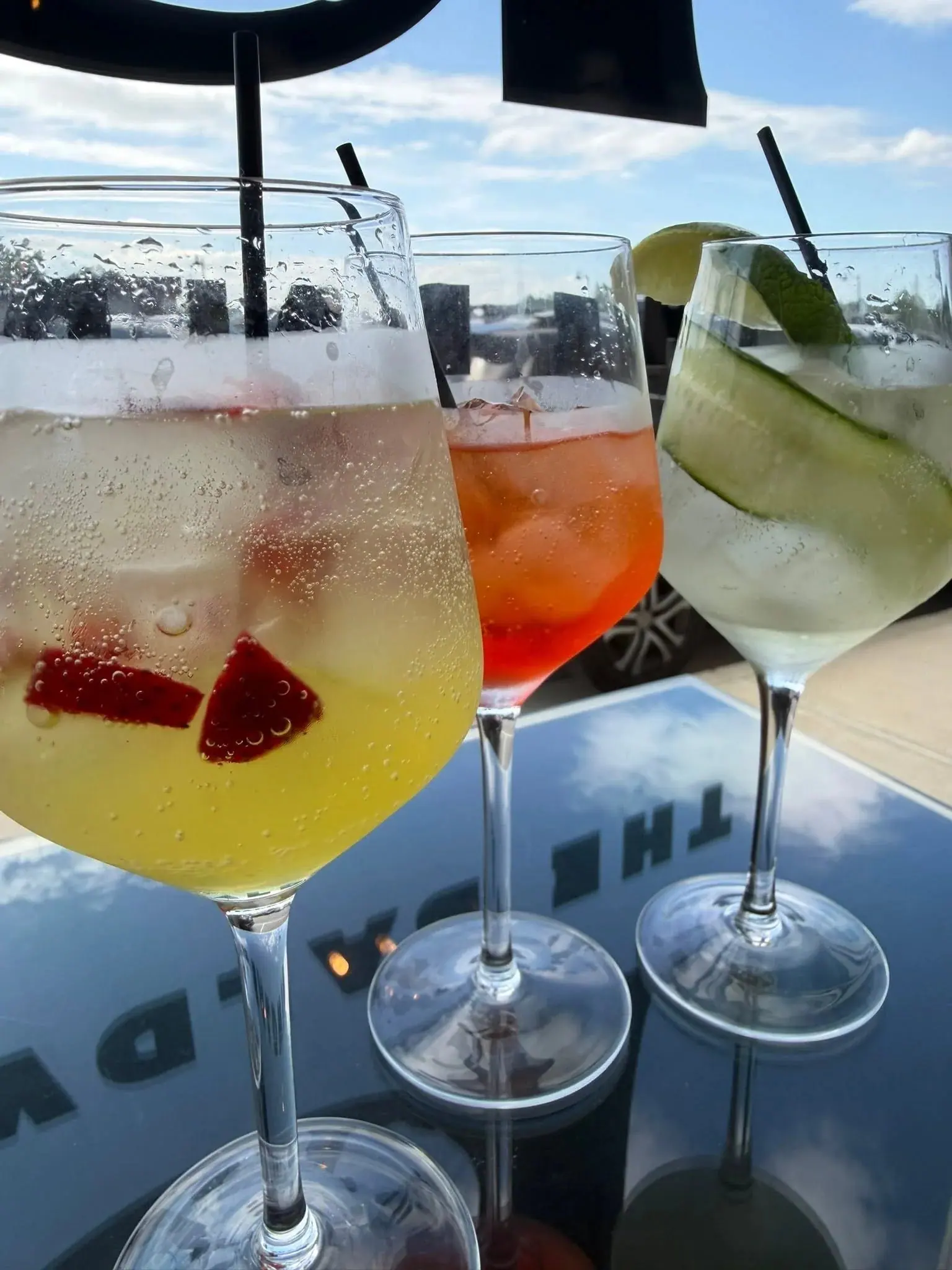 Three spritz-style cocktails in stemmed glasses on the windowsill at The Bar on Baldwin, backlit against a blue sky