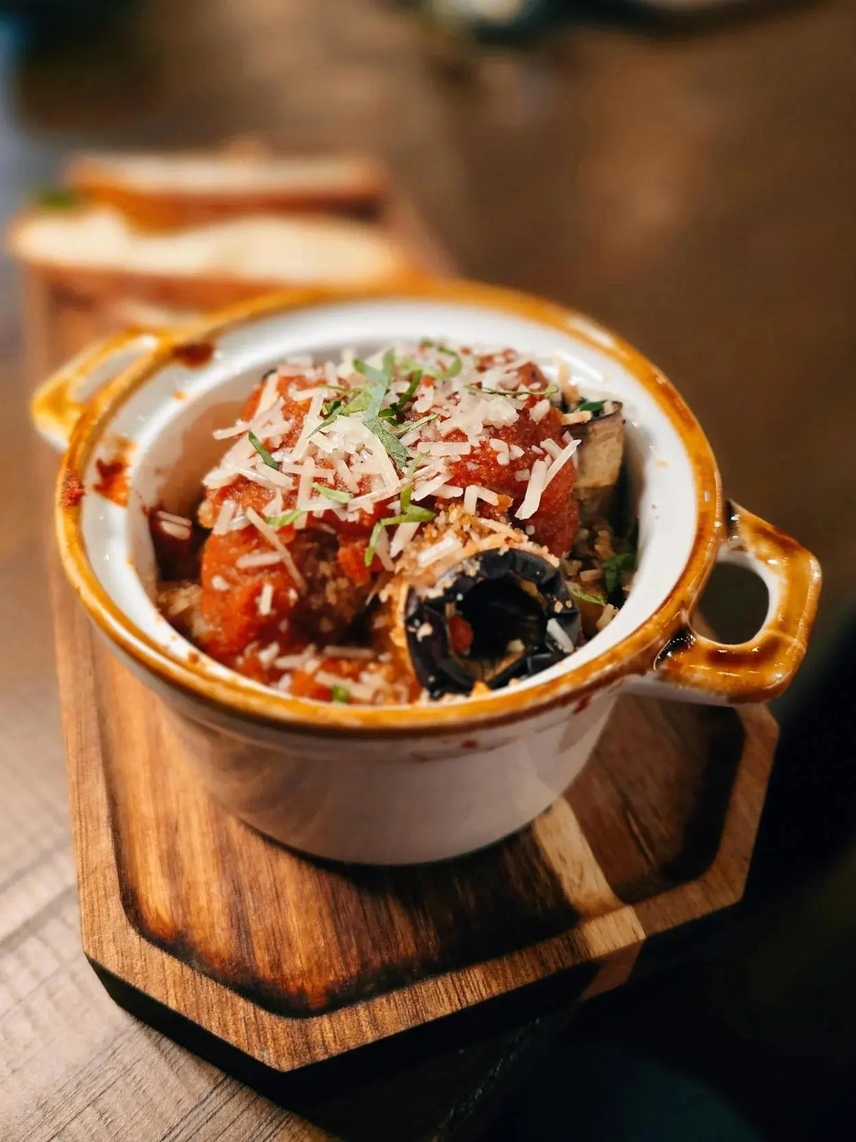 A small stoneware crock of meatballs in tomato sauce under shaved parmesan and basil