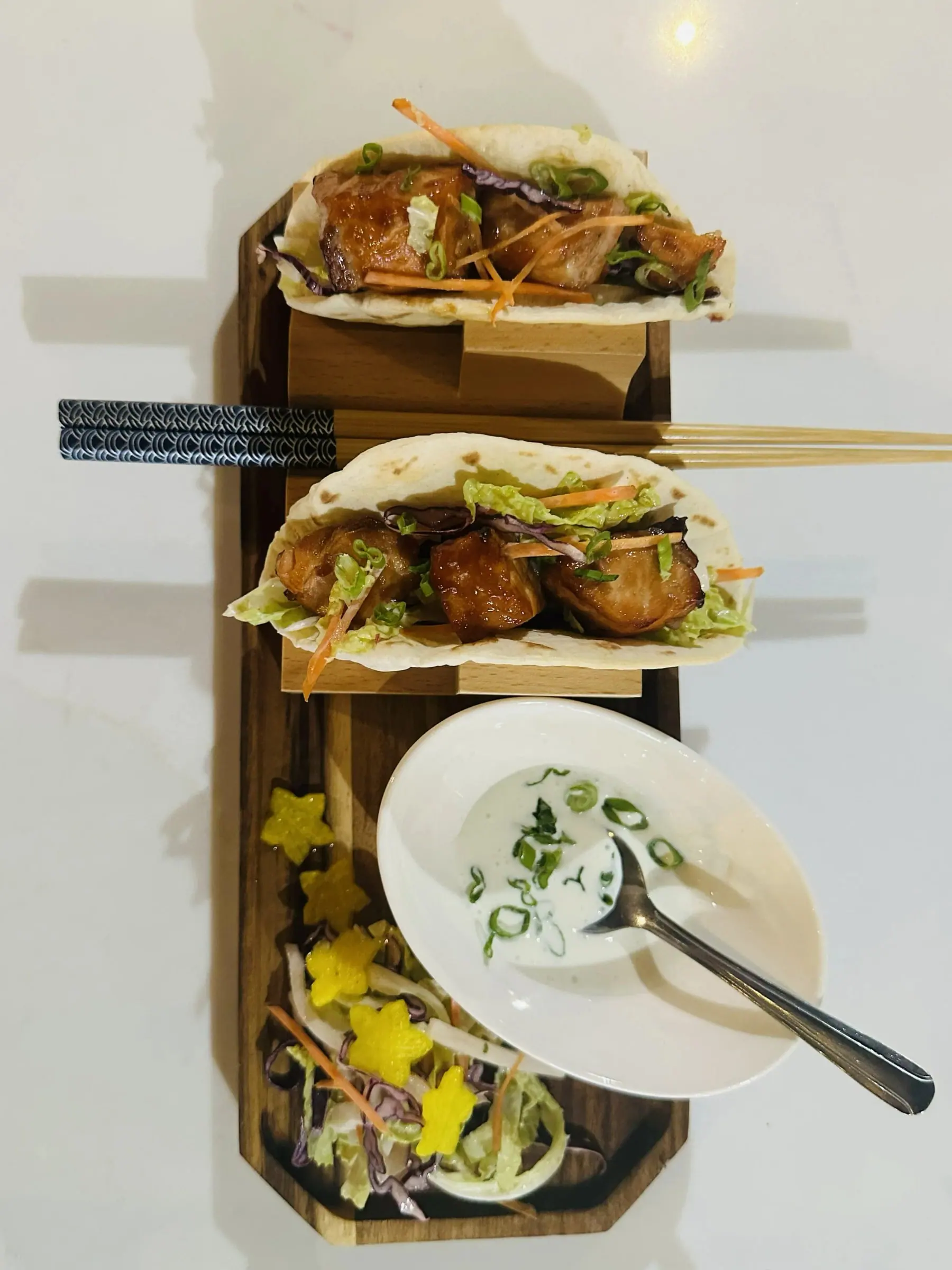 Glazed pork belly tacos on a wooden stand with slaw, pickles and a herbed dipping sauce