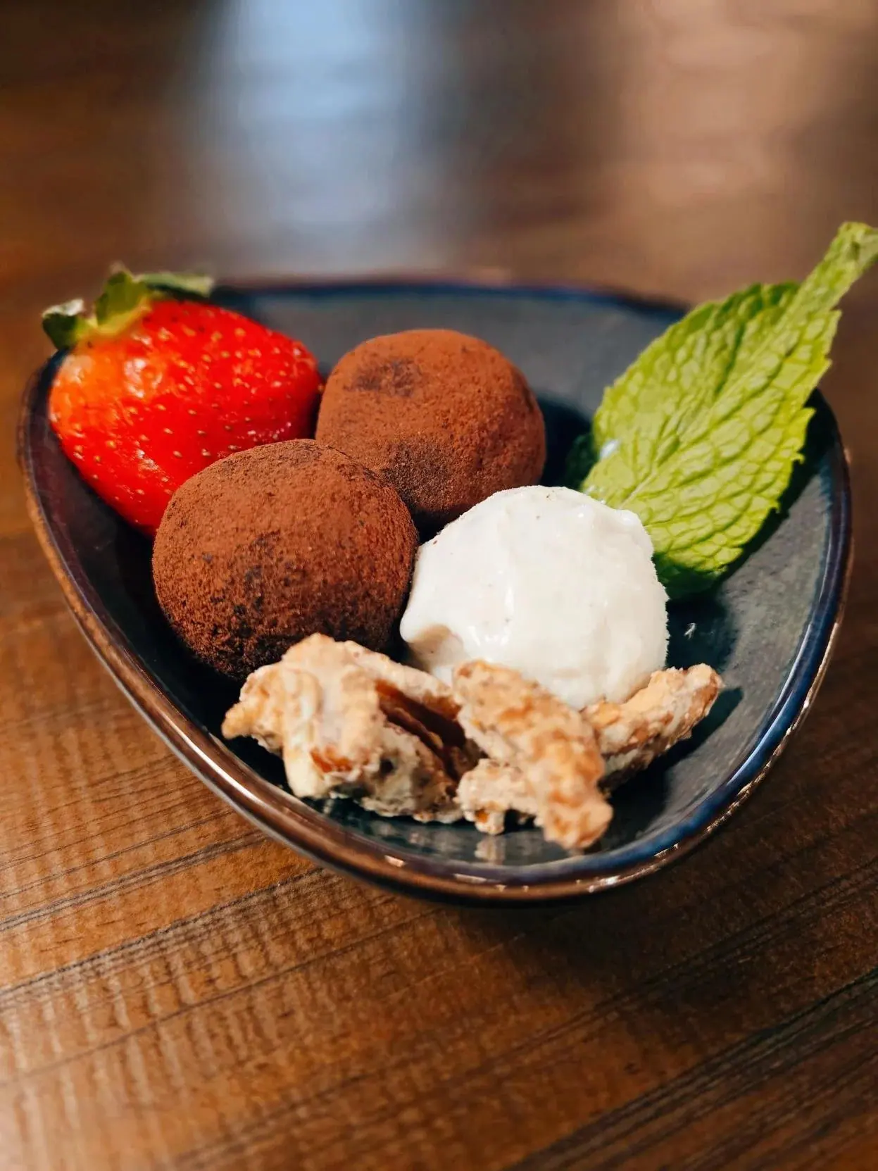 Cocoa-dusted chocolate truffles with a scoop of gelato, a strawberry and fresh mint in a dark ceramic dish
