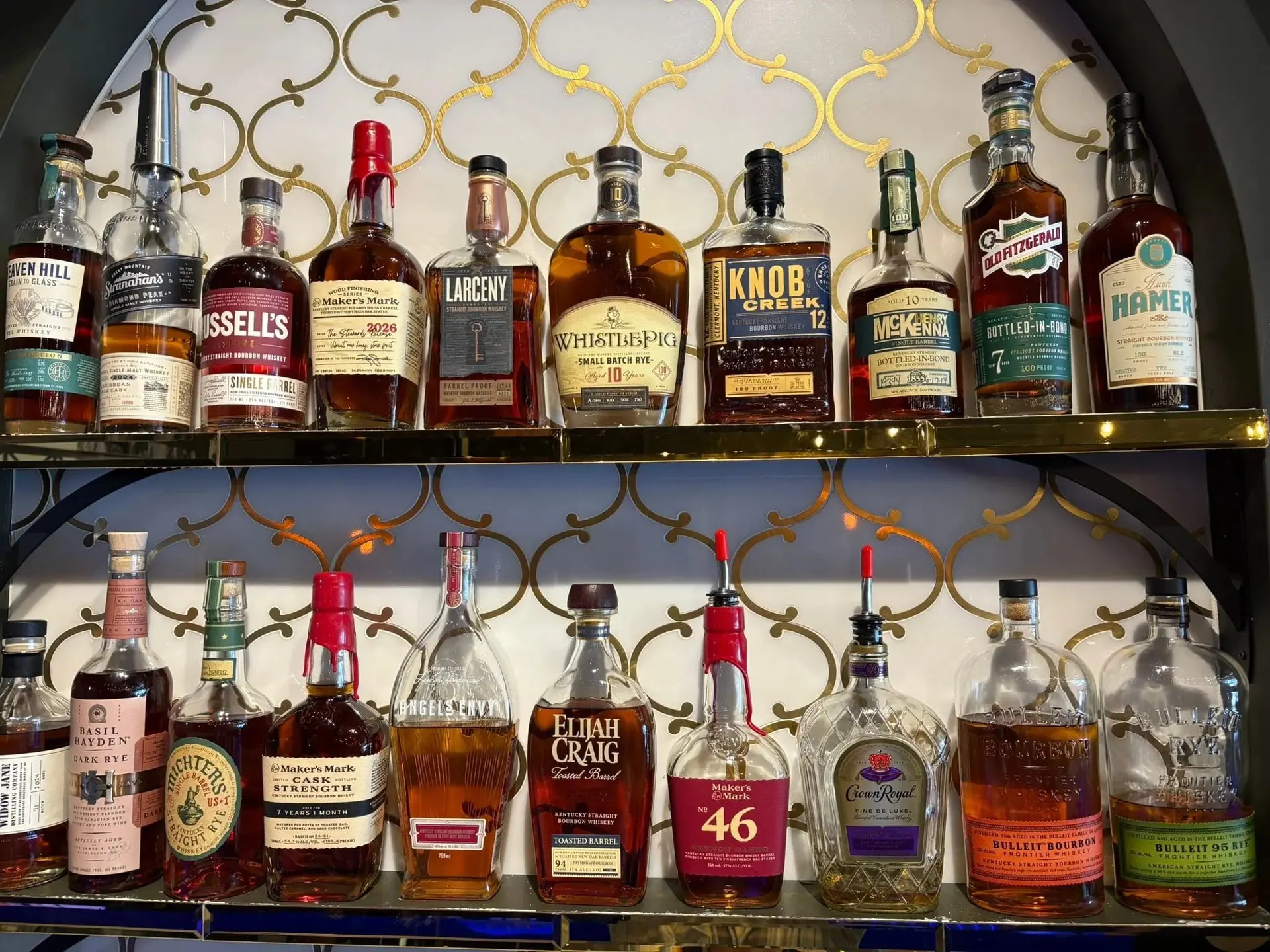 Bourbon and rye bottles lined up on the gold trellis-backed arched shelving behind the bar at The Bar on Baldwin