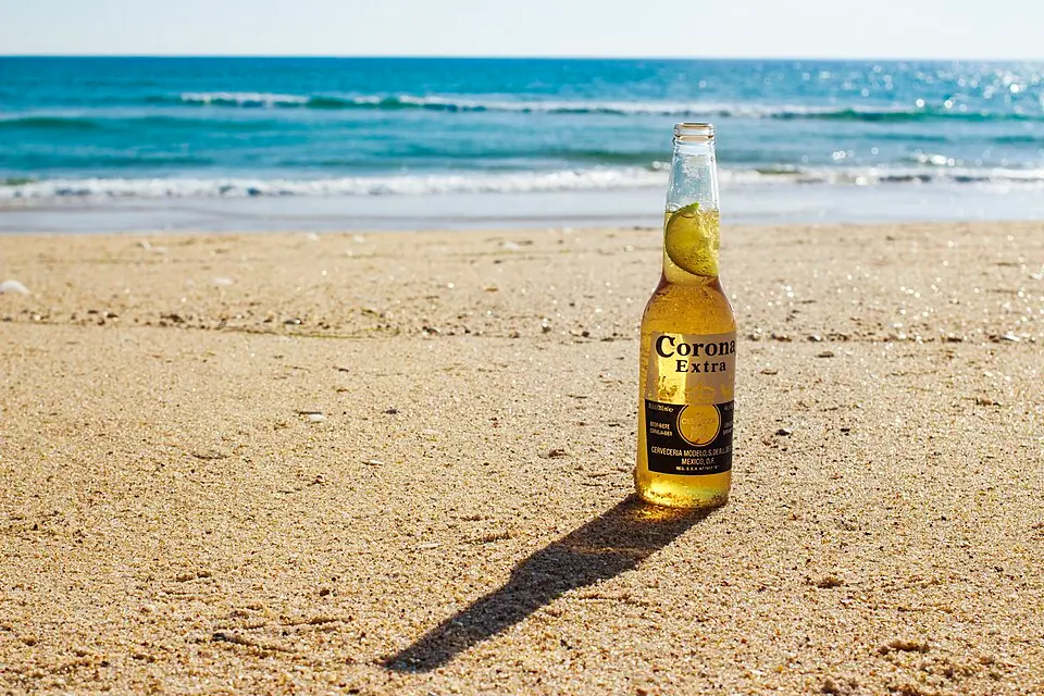 A bottle of Corona Extra with a lime wedge in the neck, standing in the sand at the beach